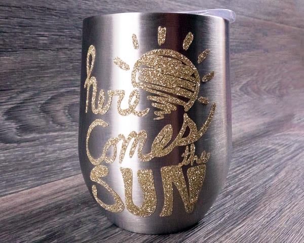 A metallic wine glass with the phrase "Here comes the sun" in Champagne Pressure Sensitive GlitterFlex Ultra