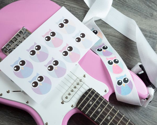 A picture of a guitar with a piece of sublimation paper and a white strap with Rainbow White Clear GlitterFlex Ultra® that have sublimated owls on it.