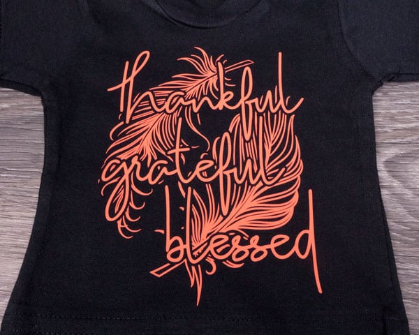 The words "thankful grateful blessed" on top of some feathers are pressed on a shirt in Dark Coral ThermoFlex® Turbo