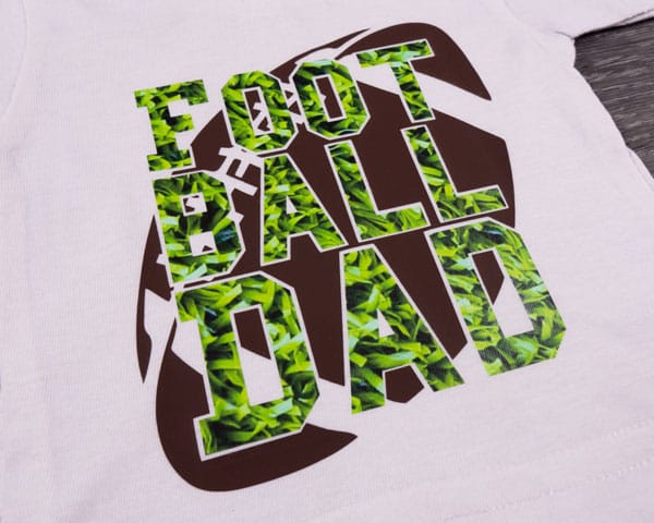 A shirt reading "Football Dad" with a football behind it made using ThermoFlex Plus and Grass ThermoFlex Fashion Patterns