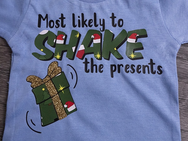 A shirt reading "Most Likely to Shake the Presents" made with ThermoFlex Plus, GlitterFlex Ultra, and Holiday Pattern ThermoFlex Fashion Patterns Festive