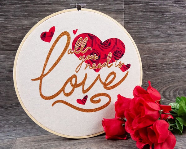 The final image of the completed hoop with "All you need is love' design using ThermoFlex® Fashion Patterns Festive and GlitterFlex® Ultra