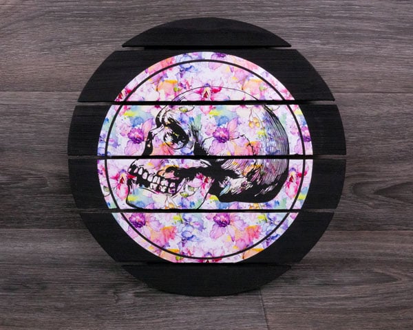 A wooden round made from planks painted black with Pastel Flowers SpecialtyPSV Fashion Patterns. A skull design is cut out in the middle.