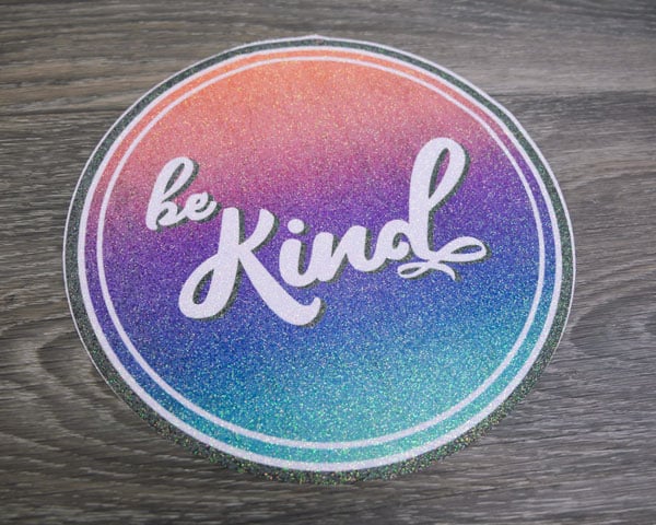 The Be Kind sublimation file pressed onto Rainbow Opaque White GlitterFlex Ultra before being pressed onto a shirt
